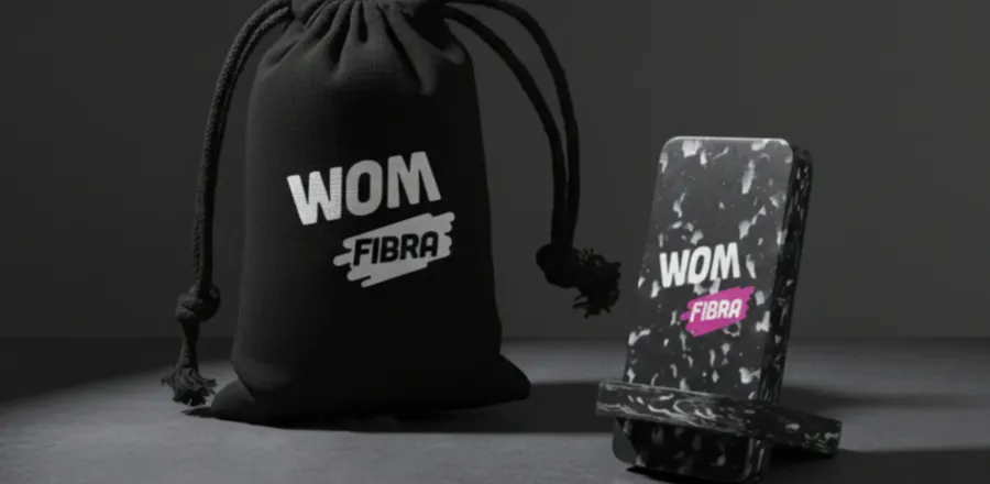 Saquito negro con logo de WOM Fibra junto a un soporte de smartphone de plástico reciclado